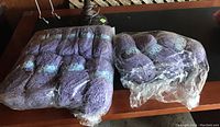Two plastic bags each containing multiple skeins of purple Sirdar Denim Chunky yarn shown on a table.