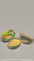 Three oval cabochon opals showing vibrant multicolored flashes on a white background, demonstrating play-of-color from different angles
