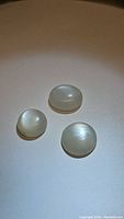 Three white moonstone cabochons with visible moonstone flash on a plain surface.