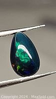 Close-up of pear-shaped black opal showing multi-color flashes held by tweezers.