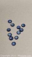 Multiple natural round cut denim blue sapphires arranged on a neutral background, showing their size and blue color.