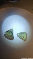 Two triangular mossy green prehnite stones illuminated to show translucency and internal rutilation inclusions.