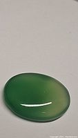 Oval green onyx cabochon gemstone lying flat on surface showing glossy and smooth polished finish.