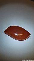 Leaf-shaped deep orange carnelian gemstone with smooth polished surface, laying flat on a white background to show shape and color.