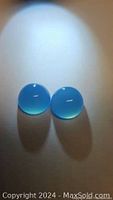 Pair of round cabochon icy blue chalcedony stones placed on a light surface showing color and translucency.
