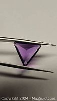 Close-up of a deep purple trillion cut amethyst gemstone held in tweezers showing its triangular shape and clarity.