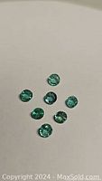 Seven round-cut green emerald gemstones arranged on a light surface, showing overall size and color.