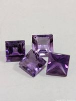Four square cut amethysts placed together showing their faceted cuts and purple color.