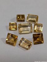 Photo of eight faceted citrine gemstones of various cuts and colors on white background