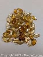 Close-up photo of multiple small faceted citrine gemstones in yellow to amber hues scattered on a white surface.