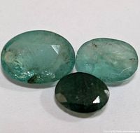 Three loose emerald gemstones of varying sizes and shades of green, photographed on white background.