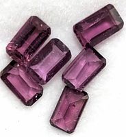 Close-up image of six rectangular-cut garnet gemstones showing their deep reddish-purple color and faceted surfaces.