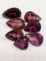 Seven pear-shaped garnet gemstones arranged on white background showing color and facets