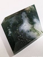 Polished green and white moss agate gemstone showing natural moss-like inclusions and a faceted irregular rectangular shape on white background.