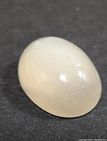 Close-up image of the polished moonstone exhibiting a smooth oval cabochon cut with translucent white color and shimmer.