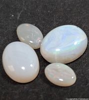 Four polished genuine opal gemstones of varying sizes on a dark textured surface, showing color play and sheen typical of opal gems.