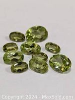 Multiple light green oval and round faceted peridot gemstones displayed on white surface showing their clarity and shape.