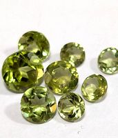 Close-up photo of eight round-cut peridot gemstones on a white background showcasing their green color and faceted cut.