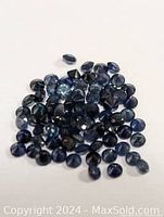 Multiple loose small round cut dark blue sapphire gemstones on white background.