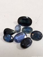 Eight loose sapphire gemstones of varying oval and pear shapes, shades of blue, on white background.
