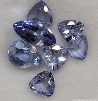 Close-up of 7 faceted loose genuine tanzanite gemstones showing various shapes and cuts, with a bluish violet appearance.