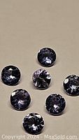 Seven round cut natural tanzanite gemstones with blue purple hues on a beige background.