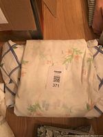 Photo showing piled bedding items including two patterned sheets and a duvet cover on a wooden floor.