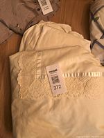 Queen size cream colored duvet folded showing scalloped lace edge and two matching pillowcases on wooden floor.