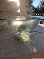 Clear glass dish with wide, shallow bowl and pedestal base shown on table backlit by sunlight.