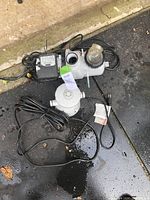 Photo showing two main pool pump components with attached cords, positioned on asphalt and concrete surface. Components are used and intended for parts.