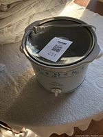 Front view of white ceramic slow cooker with floral design and glass lid on carpeted surface