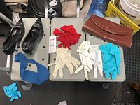 Photo showing three gray chairs with black shoes, red gloves, cream gloves, white gloves, blue gloves, brown clutch, and a small blue accessory arranged on the seats.