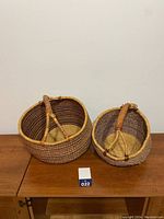 Two round woven baskets with purple and beige stripes and wooden wrapped handles placed on a wooden table.