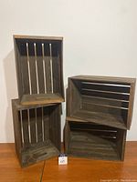 Four medium wooden crates arranged on a wooden surface showing front and inner views.