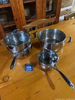 Four Lagostina cookware pieces on a wooden table including small saucepan, two medium pots, and one large pot showing handles, lids, and burn marks.