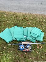 Seven green tarps folded and stacked on grass with painting supplies arranged in front