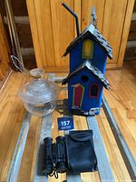 Full view of birdhouse, binoculars with case, and glass sculpture on glass table