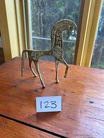 Full frontal photo of the brass horse figurine showing its slender form and base with engraved ancient symbols on the body.