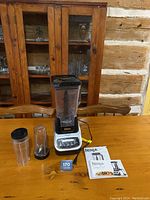 Full set including Ninja blender base, large pitcher, two Nutri-Ninja cups, instruction and recipe manuals on wooden table with rustic background.