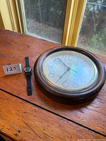 Piaget watch next to wooden wall clock on wooden surface near window, showing both items together.