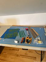 Full view of the lot arranged on the blue cutting mat: rotary cutters, rulers, stencils, tape measure, and cutting tools.