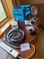 Photo showing coils of wire in different gauges, plastic crate with assorted small hardware items, can of WD-40, and vintage rusty metal handle on table.