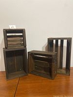 Four rustic wooden crates of varying sizes and rectangular shapes with worn finish placed on wooden table against white wall.