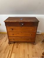 Front view of vintage wooden dresser revealing four drawers with round wooden knobs, one knob missing on second drawer, and carved rosette on top drawer