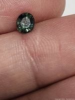 Close-up photo of a 0.54 carat oval blue teal sapphire held between fingers, showing transparency and color in natural light.