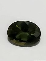 Close-up photo of the oval cut sapphire showing its dark green multicolored body and facets.