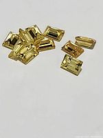 Close-up image showing multiple loose rectangular step cut yellow sapphire gemstones measuring approximately 3x2mm each, bright yellow color with good clarity.