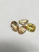 Four oval cut sapphires in yellow and orange tones displayed on white background