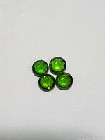 Four loose round green faceted chrome diopside gemstones placed closely together on white background, showing facets and round shape.