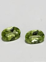 Pair of oval cut peridot gemstones displayed together showing bright green color and facets.